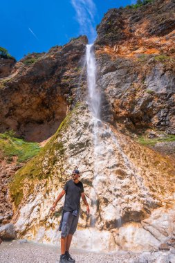 Hiker standing near the majestic rinka waterfall in logarska dolina on a sunny summer day in the kamniksavinja alps, slovenia clipart