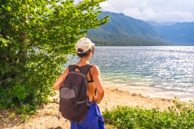 Sırt çantalı kadın turist, Slovenya 'da dağlarla çevrili Bohinj Gölü' nün yaz manzarasının tadını çıkarıyor.