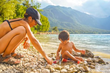 Anne ve oğul, Slovenia 'daki Bohinj gölünün manzaralı kıyılarında çakıl taşları ve oyuncak arabalarla oynayarak kaliteli vakit geçiriyorlar.