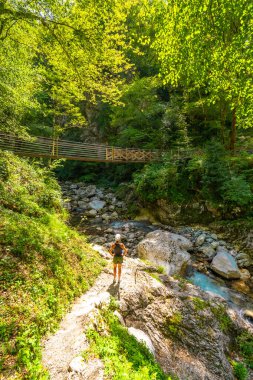 Triglav Ulusal Parkı, Slovenia 'daki nefes kesici Tolmin Geçidi manzarasının tadını çıkaran kadın yürüyüşçü, ahşap köprü ve kristal berrak Zadnja Trenta Nehri