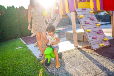 Annesi güneşli bir yaz gününde ona göz kulak olurken küçük çocuk arka bahçede motorsiklet sürmekten hoşlanıyor.