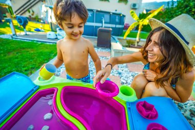 Anne ve oğul birlikte güzel vakit geçiriyorlar, yaz tatillerinde arka bahçelerinde renkli bir su tablosuyla oynuyorlar.