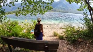 Bohinj Gölü 'nün manzaralı güzelliğinin tadını çıkaran bir aile göl kenarında geziyor, güneşli bir yaz gününde manzaralı dağ manzaralarını ve kristal berrak suları seyrediyor.