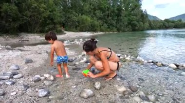 Anne ve oğul yaz tatillerinin tadını çıkarıyor, Slovenia 'daki güzel bir gölün kıyısında çakıl taşlarıyla oynuyorlar.