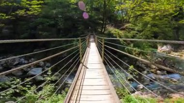 Güneşli bir yaz gününde yemyeşil yeşilliklerle çevrili Tolmin Vadisi, Slovenia 'daki berrak bir dereden tahta asma köprüsü geçiyor.