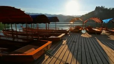 Göldeki rıhtıma demirlemiş ahşap turist tekneleri. Kanlı bir ada, arka planda ikonik bir kilise ve parlayan güneşle birlikte Slovenia 'da kanadı.