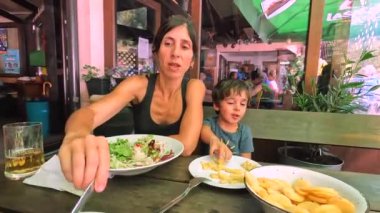 Anne ve oğlu deniz kenarındaki bir restoranda öğle yemeği yiyorlar. Birlikte yaz tatilinin tadını çıkarıyorlar.