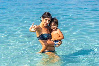 Bir kadın ve bir çocuk okyanusta, kadın çocuğu tutuyor. Sahne mutlu ve neşeli.