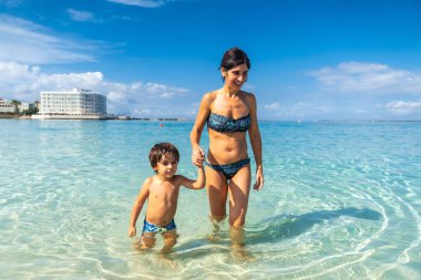 Anne ve oğul el ele tutuşup Mallorca, İspanya 'da yaz tatillerinde Estanys sahilinin turkuaz suyunun tadını çıkarıyorlar.