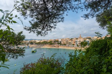 Puerto Koyu 'nu kumlu sahili, binaları ve kilise kulesiyle çevreleyen yemyeşil bitki örtüsü güneşli bir yaz gününde feribot kalkıyor.