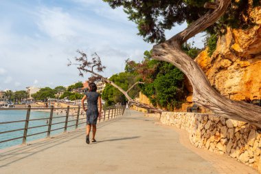 Turist Puerto Cristo, Mallorca, İspanya 'da sahil kenarında yürüyüş yapıyor. Arka planda plaj ve kasaba var.