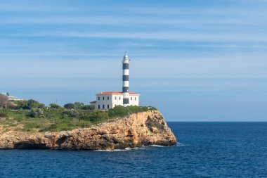 Siyah ve beyaz çizgili deniz feneri, açık mavi gökyüzü ile Mallorca, İspanya sahilinde bir uçurumda duruyor.