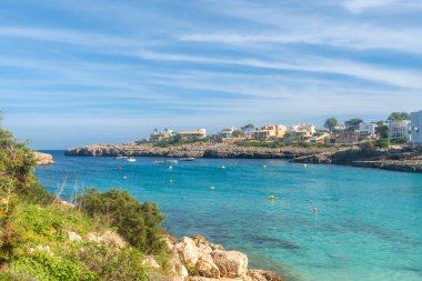 Sakin turkuaz sular, parlak mavi bir gökyüzünün altında kayalık sahil kenarına kurulmuş lüks villaları olan Cala Domingos sahiline nazikçe yaklaşır.