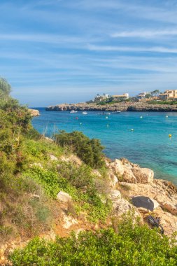 Sakin Cala Domingos plajında, Mallorca, İspanya 'daki kayalık sahil şeridi boyunca yemyeşil ve lüks villalarla çevrili turkuaz sularda yatlar bulunur.