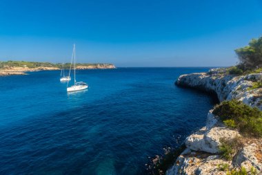 Beyaz yelkenliler kristal berrak turkuaz sularına demirlediler Cala s 'amarador körfezinin kayalık kayalıklar ve yemyeşil sularla çevrili.
