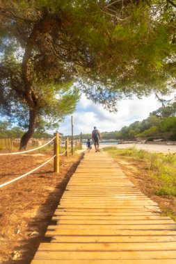 Güneşli bir yaz günü Mallorca, İspanya 'da güzel plajlara giden ahşap yolda yürüyen turistler.