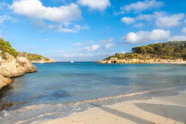 Mallorca, İspanya 'daki s' amarador sahilinin güzel manzarası, durgun turkuaz su, beyaz kum, kayıklar, yeşil ağaçlar ve bulutlu kayalar.