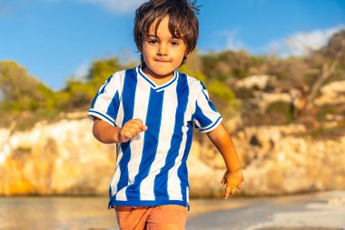 Yaz tatilinde Mallorca, İspanya 'da s' amarador plajında koşan mavi beyaz çizgili tişört giyen genç bir çocuk.