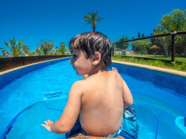 Genç bir çocuk güneşli bir yaz gününde, bir su parkında, tembel bir nehirde yüzüyor ve eğleniyor.