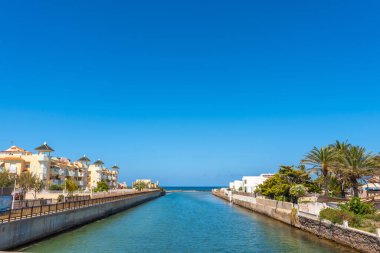 Calm canal flowing to the sea between residential buildings in la manga del mar menor, a touristic coastal strip in murcia, spain clipart