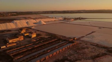 Torrevieja pembe gölünün tuz buharlaşma göletleri üzerinde gün batımında büyük tuz yığınları ile kamera görüntüsü.