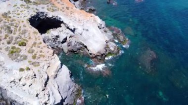 Yaz güneşinin tadını çıkaran turistler kayalık bir uçurumun altındaki kumsalda büyüleyici bir doğal kemere sahipler.