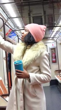 Yeniden kullanılabilir bardaktan sıcak bir yudum yudumlayan şık genç bir kadın yoğun saatlerde şehir metrosunda gidip geliyor.