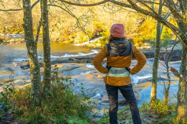 Güneşli bir sonbahar gününde Gorbeia Doğal Parkı 'ndaki Baias Nehri manzarasının tadını çıkaran kadın yürüyüşçü.