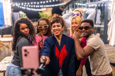 Çok ırklı arkadaşlar bir barın terasında kutlama yaparken selfie çekiyorlar.