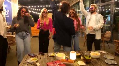 Beyaz kadın, açık hava partisinde bira içip çok ırklı arkadaşlarla dans ediyor.