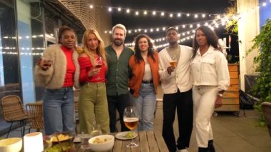 Çok ırklı bir insan grubunun portresi. Terasta oturmuş, içki bardaklarıyla kameraya gülümsüyorlar.