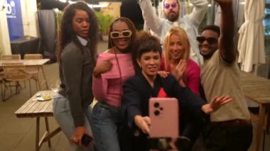 Çok ırklı arkadaşlar bir barın terasında kutlama yaparken selfie çekiyorlar.