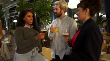 Çok ırklı arkadaşlar bira içerek ve açık hava gece terasında sohbet ederek eğleniyorlar.