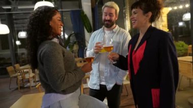 Çok ırklı üç mutlu arkadaş bir gece barının terasında kutlama yapıyor.