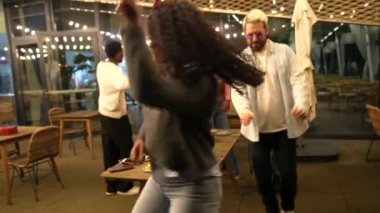 Latin bir kadın gecenin bir yarısı çeşitli arkadaşlarıyla bir çatı barında eğlenirken mutlu bir şekilde dans ediyor.