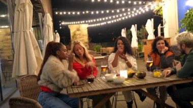 Çok ırklı arkadaşlar bir bar terasında oturup geceleri birlikte kutlama yapıyorlar.