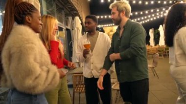 Bir barın çatısında bira içerken çok ırklı mutlu arkadaşlar konuşuyor.