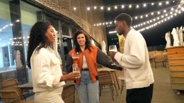 Çok ırklı arkadaşlar gece bir barın zarif çatı terasında bira içerken konuşuyorlar.