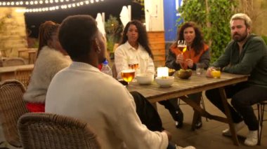 Barın terasında oturmuş, geceleri rahatça sohbet eden çok ırklı arkadaşlar.