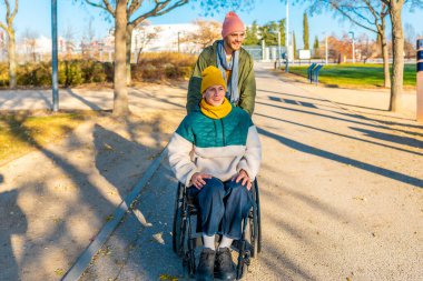 Parkta güneşli bir günün tadını çıkaran gülümseyen arkadaşlar, hayat dolu ağaçlarla çevrili yolda yürürken kahkahalarınızı ve sıcaklığınızı paylaşın.