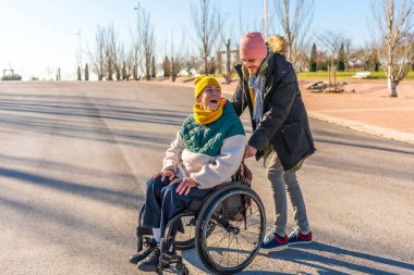 Genç bakıcı mutlu, yaşlı bir kadına tekerlekli sandalyede yardım ediyor güneşli bir kış gününün tadını çıkarıyor.