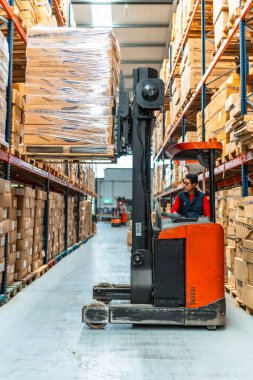 Dağıtım deposunda forklift kullanan Latin bir işçinin dikey boy fotoğrafı.
