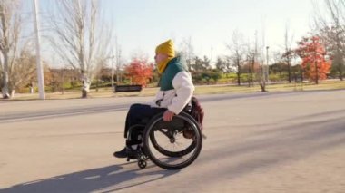 Parkta güneşli bir günün tadını çıkaran engelli kişi tekerlekli sandalyesinde özgürce dolaşıyor.