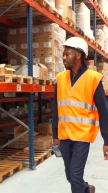 Güvenlik yeleği ve kask giyen lojistik işçisi depo ortamında malları tarayıp kontrol ediyor.