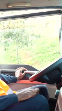 Genç kamyon şoförü yolculuk için hazırlanıyor, koltuğu, aynaları ayarlıyor ve kabinin içini kontrol ediyor.