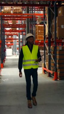 Güvenlik yeleği ve kask giyen lojistik operatörü depoya giriyor ve envanteri kontrol ediyor.