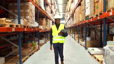 Depo koridorlarında yürüyen lojistik operatörü, mal ve malları kontrol ediyor.