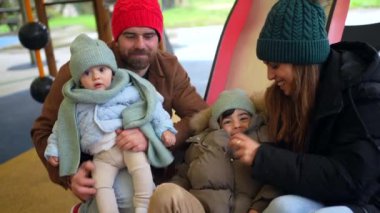 İki çocuklu mutlu bir aile, bir bebek ve bir bebek, soğuk bir kış günü oyun alanında birlikte eğleniyorlar.