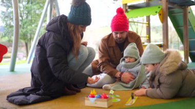 Mutlu bir aile, parkta serin bir kış günü birlikte vakit geçirip masa oyunu oynuyor.