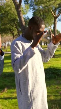 Genç Afrikalı Müslüman erkek huzur parkında geleneksel namaz kılıyor, dashiki giyiyor, açık havada yeşil manzaralı ve mavi gökyüzü boyunca ayakta duruyor.
